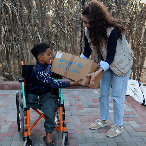 En gutt i rullestol mottar en pakke med klær fra en UNICEF-ansatt, Gaza