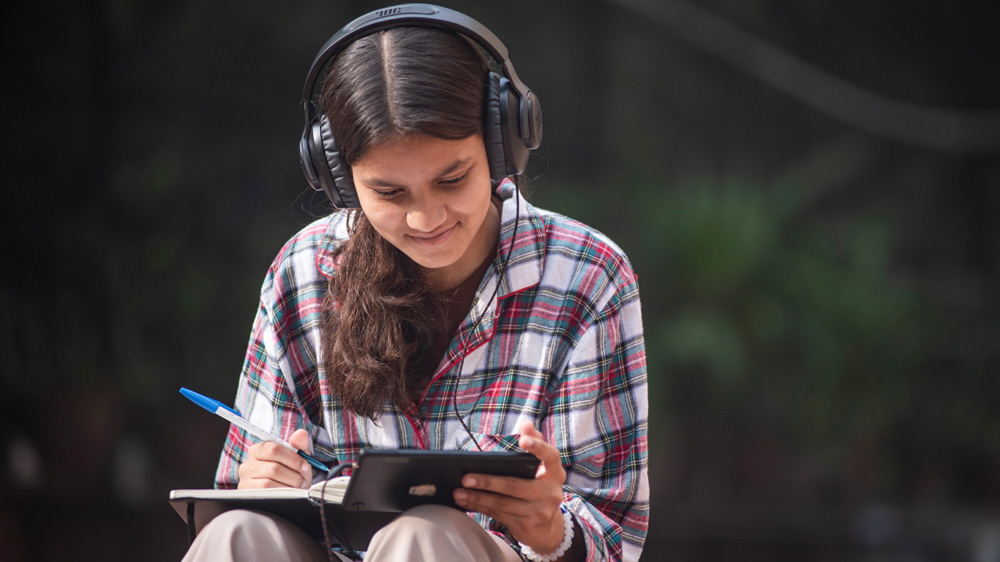 En ungdom sitter med et nettbrett og hodetelefoner, India