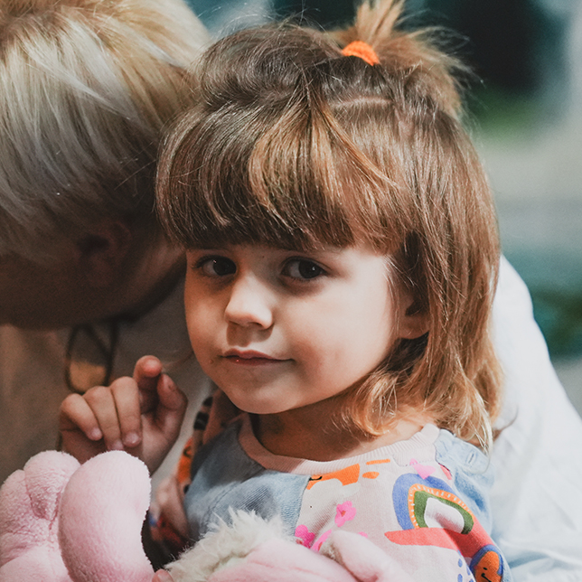 Jente som sitter på fanget til en omsorgsperson. FOTO