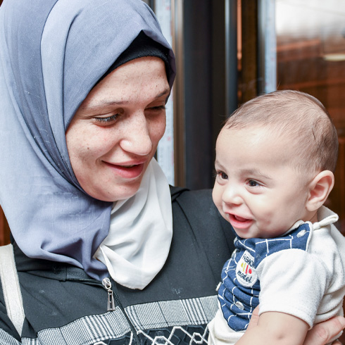 En mor holder sin tre måneder gamle sønn utenfor et helsesenter i Syria