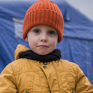 En gutt holder en lekelastebil foran store blå telt, Romania